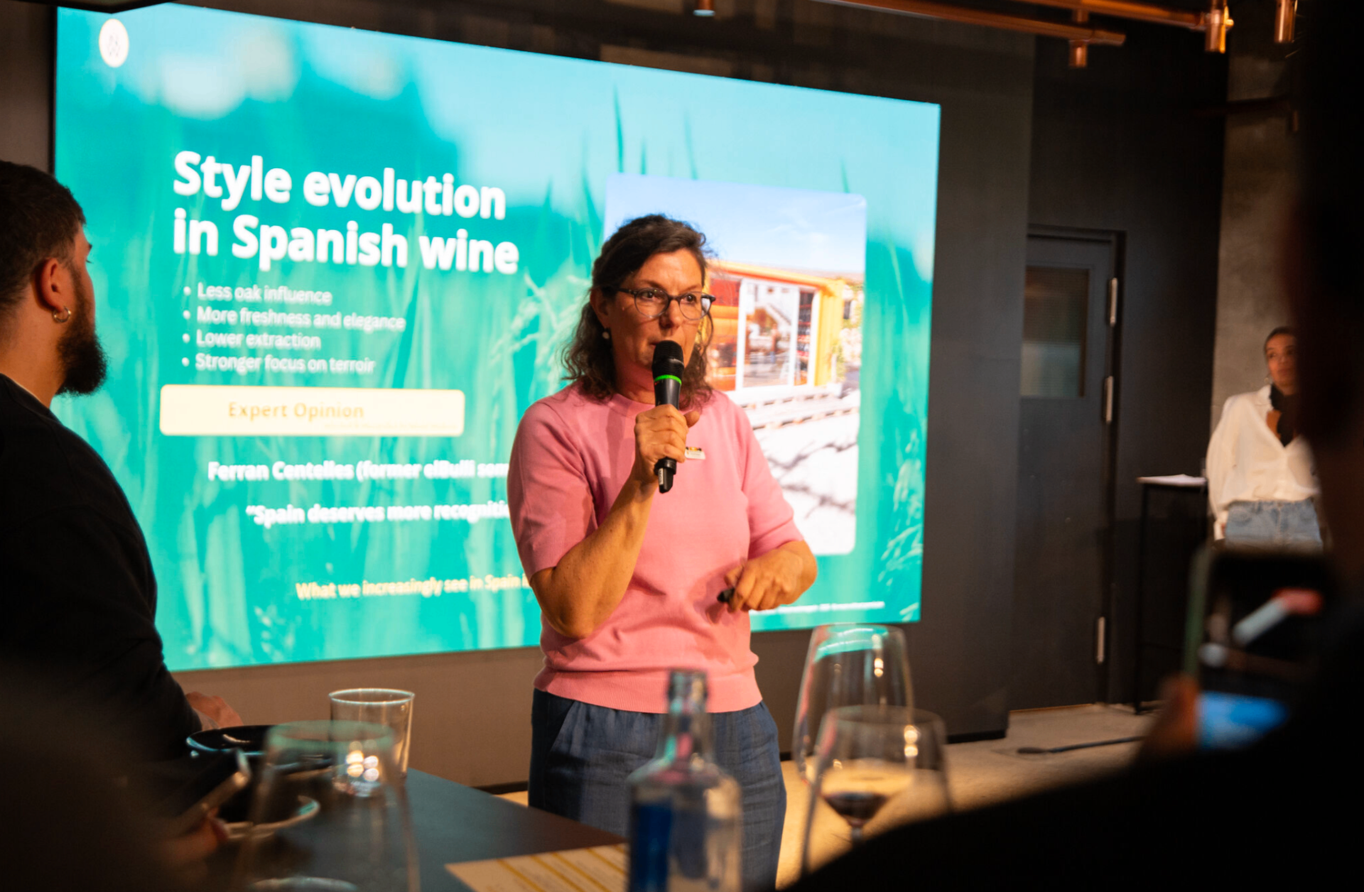 Nicole Wolbers speaking with a microphone in front of a presentation on Spanish wine to a live audience